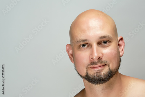 Attractive smiling bald man on gray background in studio