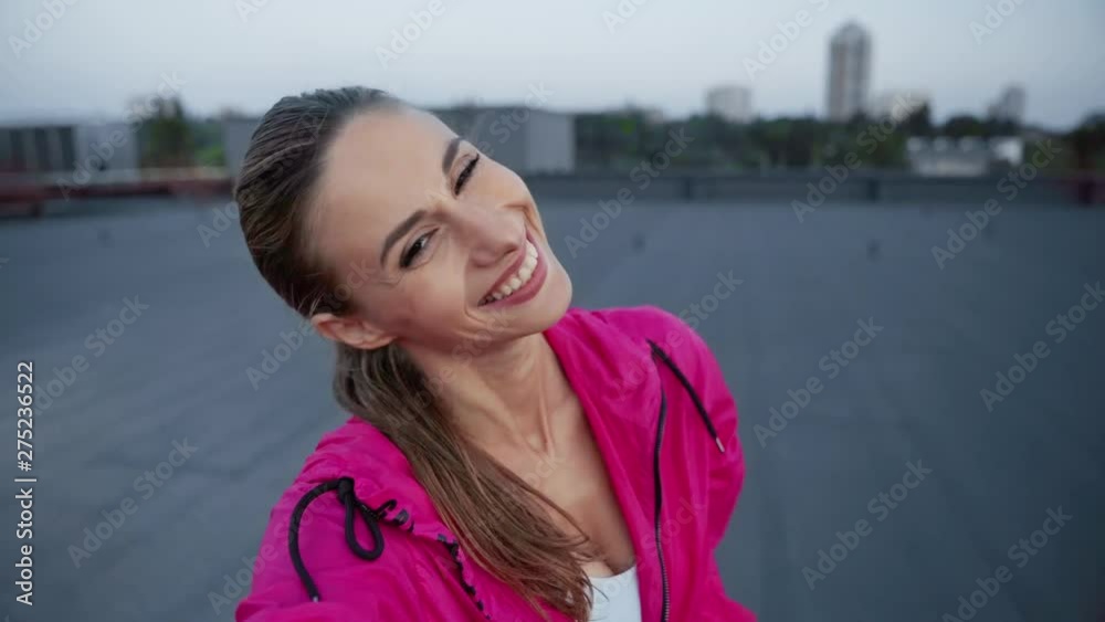 charming sportswoman in sportswear waving hello, talking at video chat, holding smartphone in hands and standing on rooftop charming sportswoman in sportswear waving hello, talking at video chat, holding smartphone in hands and standing on rooftop