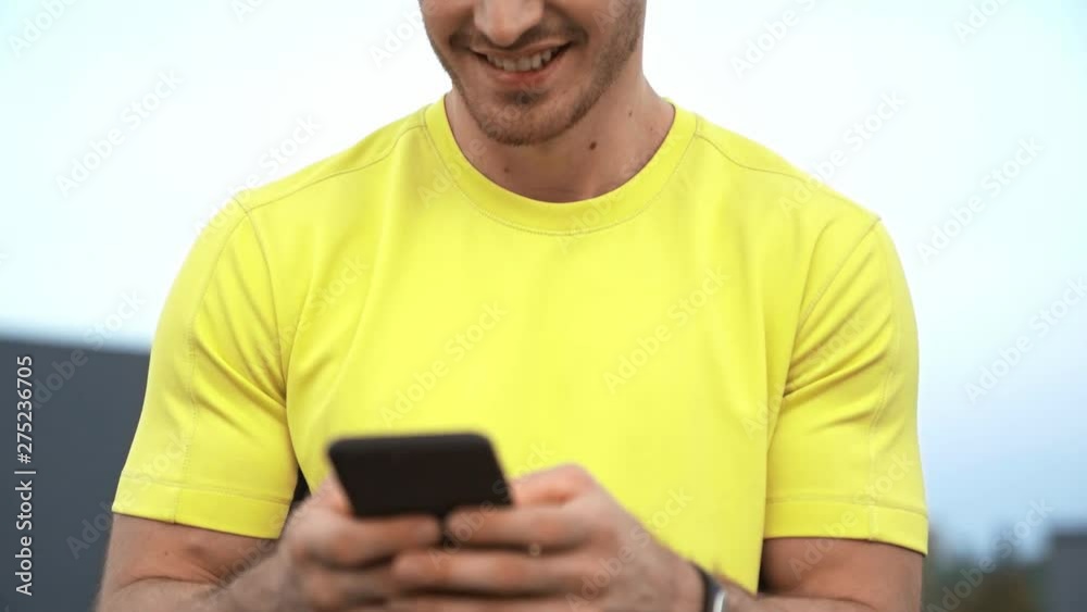 low angle view of sportsman in yellow sportswear sitting on rooftop, holding smartphone in hands, texting message, smiling and making serious face low angle view of sportsman in yellow sportswear sitting on rooftop, holding smartphone in hands, texting message, smiling and making serious face