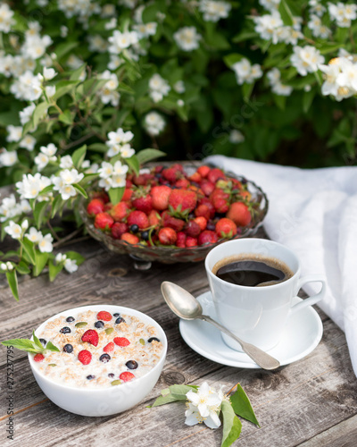 Granola with oatmeal milk with strawberries for breakfast in the summer garden. Morning at the cottage. Cup of coffee.