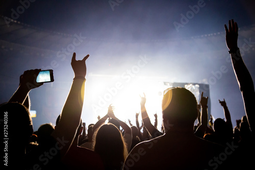 Silhouette of a concert crowd. The audience applauds the musicians on stage. The bright spotlight and dancing people.