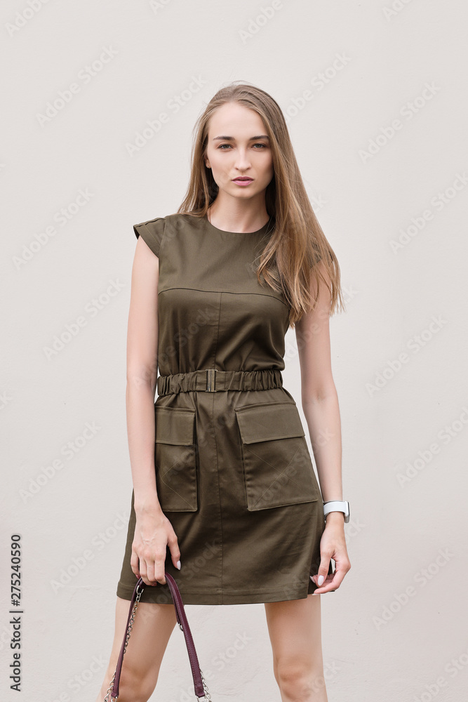 Pretty girl in military style khaki dress posing near the wall of house Pretty girl in military style khaki dress posing near the wall of house
