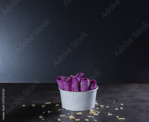 Delicious rolled Thai violet ice cream on dark table with dark background and almond chips