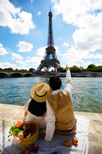 Young couple is travel in Paris and looking at eiffle tower at river side as for pre-wedding photograph. photo