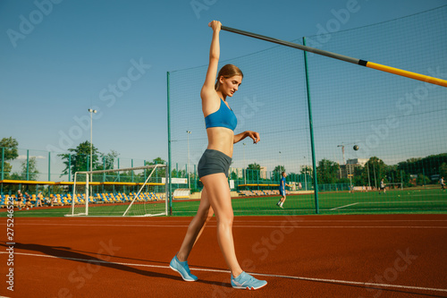 Professional female pole vaulter training at the stadium in sunny day. Fit female model practicing in high jumps outdoors. Concept of sport, activity, healthy lifestyle, action, movement, motion.