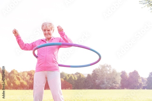 Senior woman doing gymnastic with hula hoop in park photo