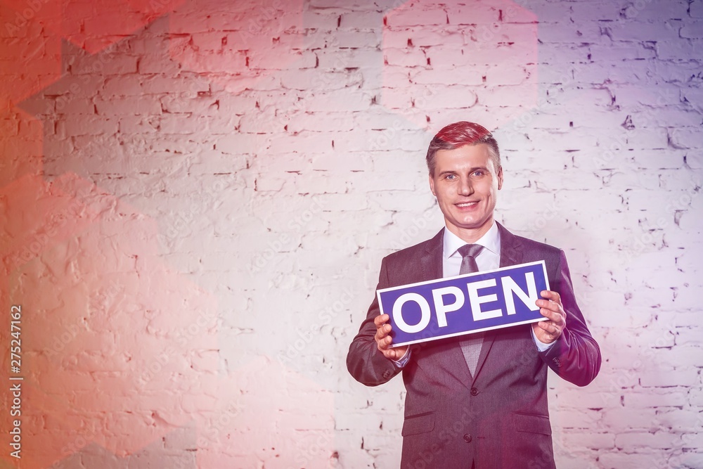 Portrait of smiling mature businessman holding open sign against brick wall at office Portrait of smiling mature businessman holding open sign against brick wall at office