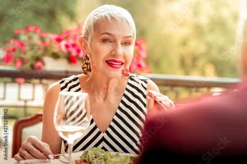 Mature woman with bright pink lips eating salad and talking to husband