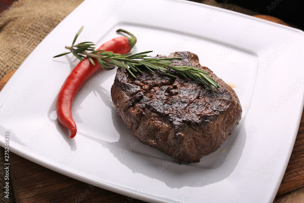 Well-done steak with chili pepper and cherry tomatoes on a wooden dish. Food photo for restaurant menu