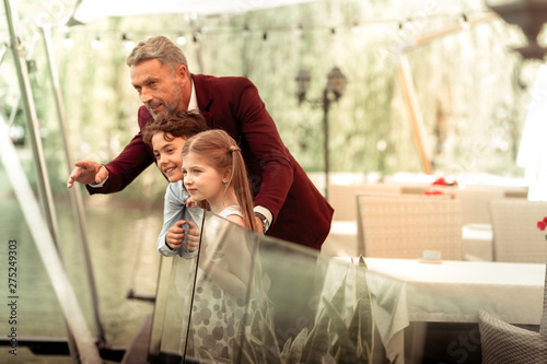 Children standing near father on summer terrace and looking at lake