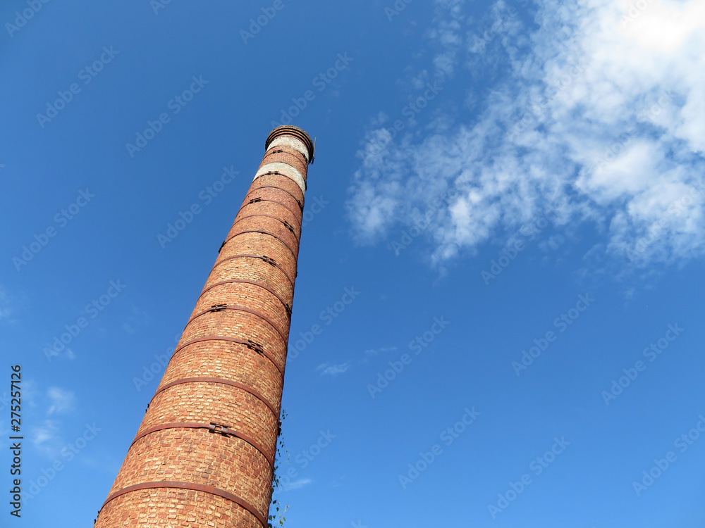 Red brick pipe on the background of blue sky with white clouds, bottom view. Concept of environmentally friendly production, inactive factory chimney and ecology, air pollution