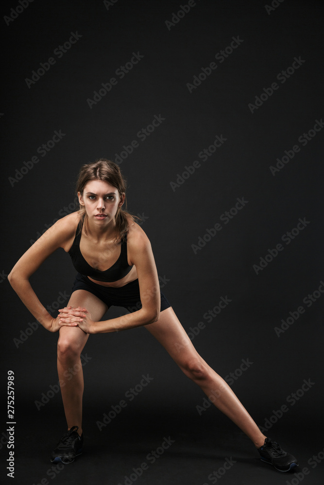 Full length portrait of gymnastic caucasian woman in sportswear stretching her legs during workout in gym