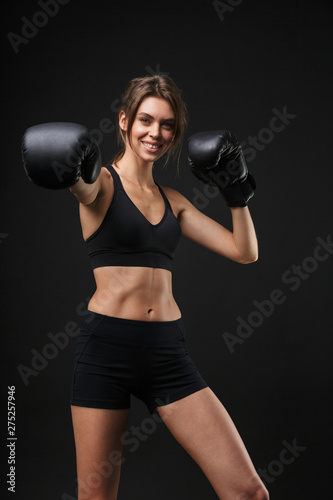 Portrait of smiling caucasian woman in sportswear posing at camera with boxing gloves during workout in gym