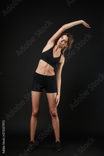 Full length portrait of young caucasian woman in sportswear stretching and bending her body during workout in gym