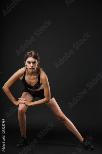 Full length portrait of gymnastic caucasian woman in sportswear stretching her legs during workout in gym