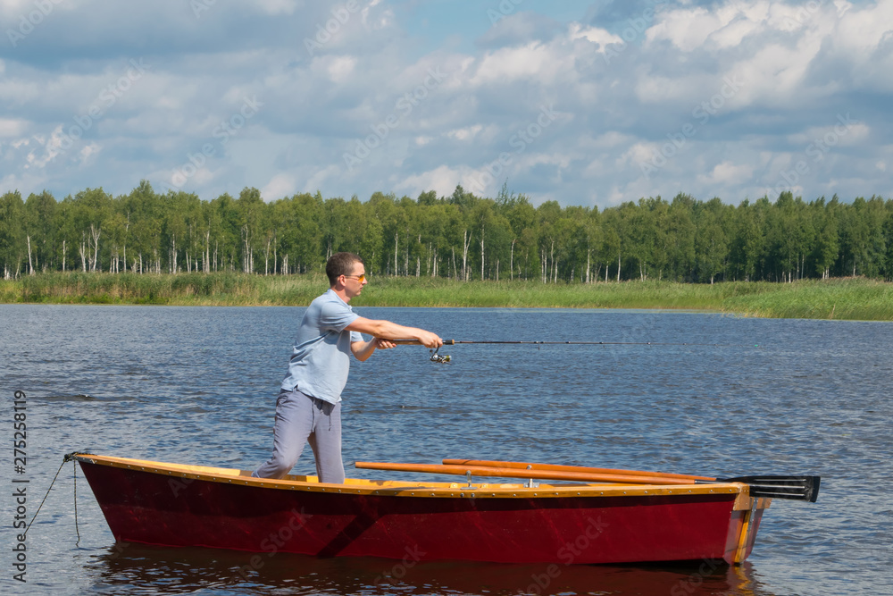 a man in yellow glasses, in a boat with oars, in the center of the lake, holds a fishing pole to catch a big fish, amid a beautiful landscape