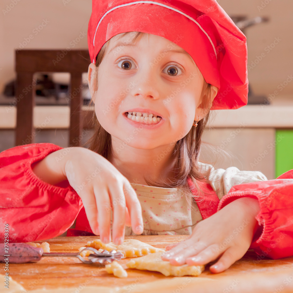 Children cooking. Little funny child girl in chef hat playing with dough and having fun in kitchen.