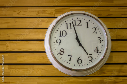 large white round clock close-up with arrows on a yellow wooden plank wall. horizontal lines. natural texture surface