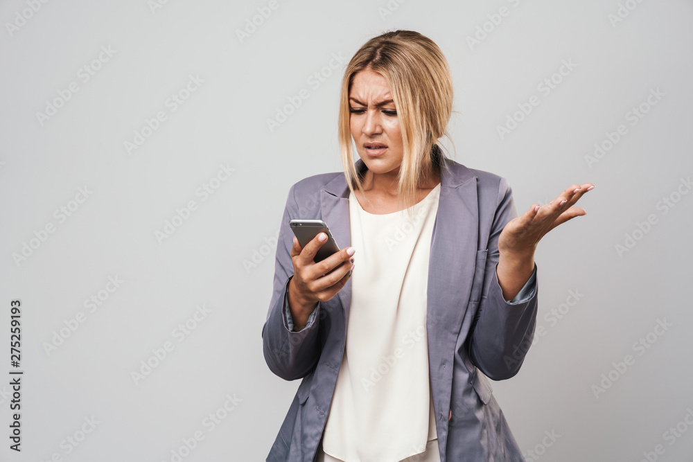Amazing confused young pretty woman posing isolated over grey wall background using mobile phone. Amazing confused young pretty woman posing isolated over grey wall background using mobile phone.