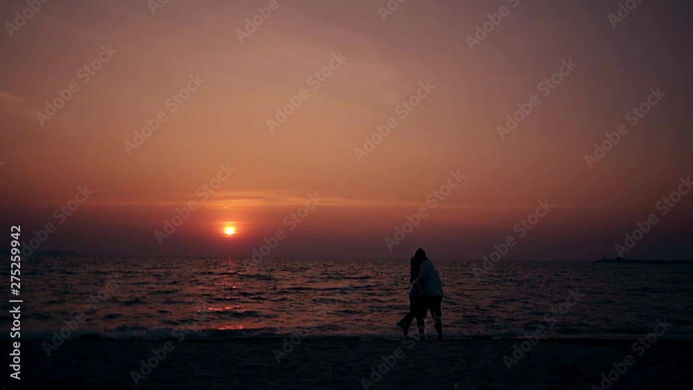 silhouettes of couple hugging and kissing on empty evening beach against ocean waves and red sun slow motion silhouettes of couple hugging and kissing on empty evening beach against ocean waves and red sun slow motion