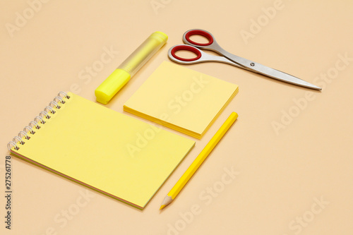 Scissors, pencil, notebook, note-paper and yellow felt-tip pen on beige background.