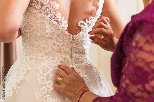 mother helps the bride to clothe her wedding dress. fastening a wedding dress to a bride.