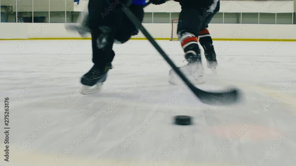 Low-section shot of hockey players skating on ice arena with puck while one catching another with stick and he falling down and missing puck