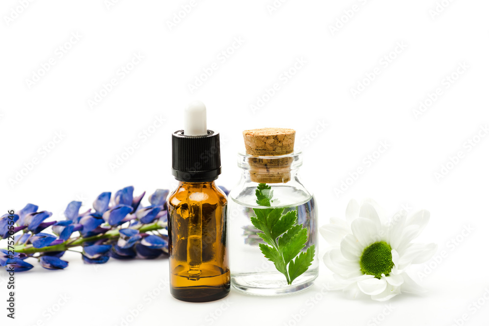 selective focus of bottles with liquid near flowers isolated on white selective focus of bottles with liquid near flowers isolated on white