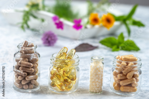 Herbal supplements and vitamins on wooden tray , decorated with colorfull medicinal flowers and herbs blurry wooden background
