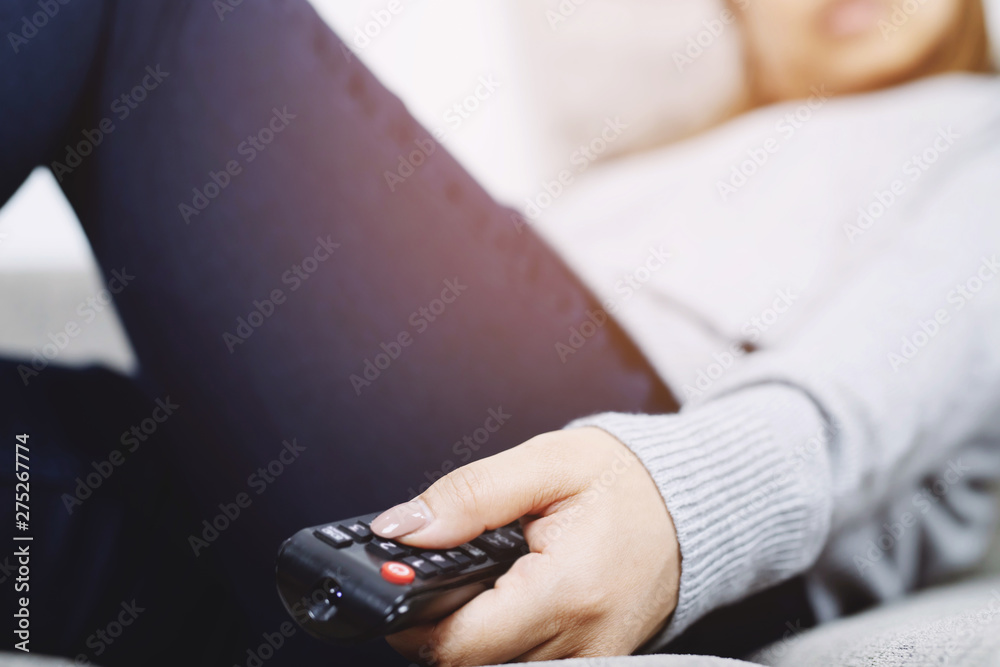 close up Television remote control in casual young female hands pointing to tv set and turning it on or off. select channel watching tv sleep on sofa at home in the living room relax. close up Television remote control in casual young female hands pointing to tv set and turning it on or off. select channel watching tv sleep on sofa at home in the living room relax.