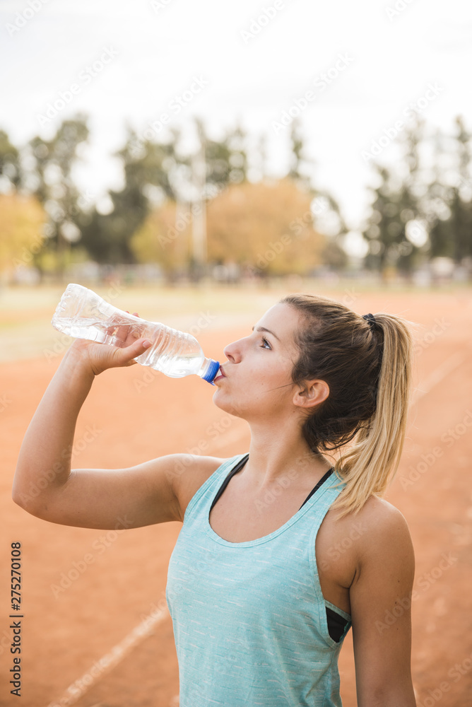 Sporty woman drinking on stadium track Sporty woman drinking on stadium track