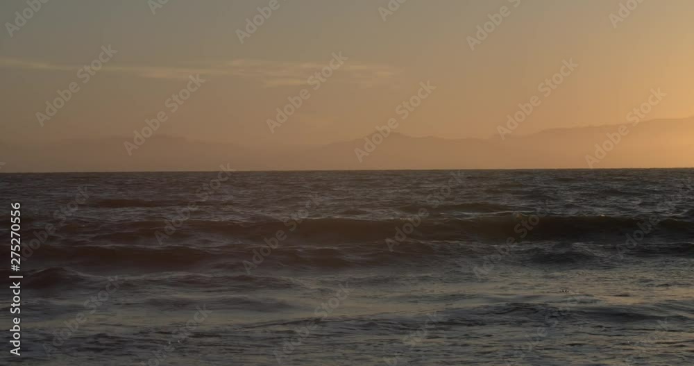 Waves crashing on beach at sunset in San Francisco Bay area with Marin Headlands in the background in slow motion Waves crashing on beach at sunset in San Francisco Bay area with Marin Headlands in the background in slow motion