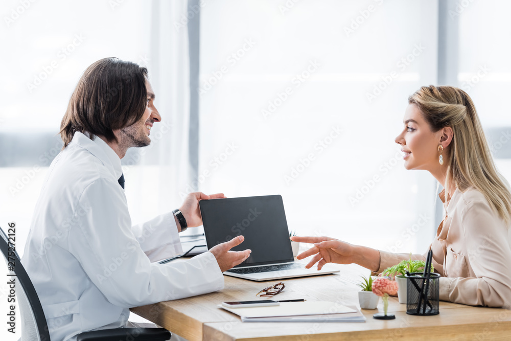 happy patient looking at doctor and pointing with finger on laptop in hospital happy patient looking at doctor and pointing with finger on laptop in hospital
