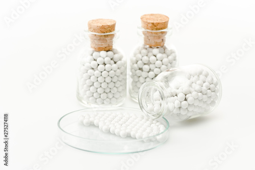 selective focus of round pills in glass petri dish near bottles with wooden corks isolated on white