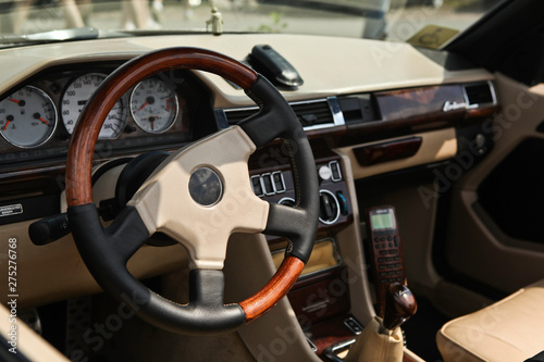 Old style classic luxury car interior. Steering wheel in focus, close up view. Natural skin and expensive elements coating. Old mobile phone, gear shift knob, glove box blurred in the background.