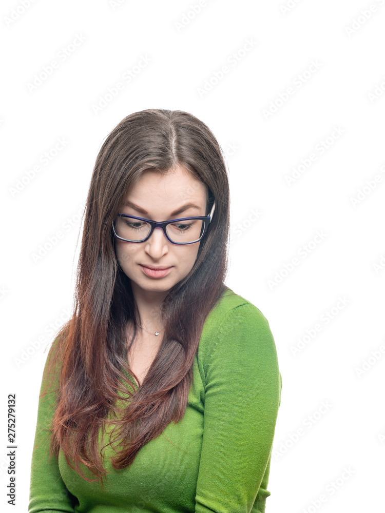 Young woman portrait. Long hired brunette female person in glasses and green blouse looking down with skeptical emotion on her face. Vertical image isolated on white background. 