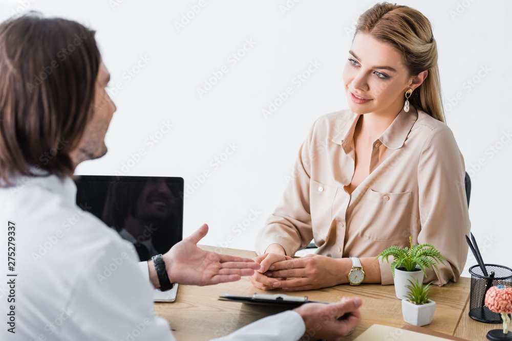 doctor talking with patient, holding document in hands and sitting behind wooden table doctor talking with patient, holding document in hands and sitting behind wooden table