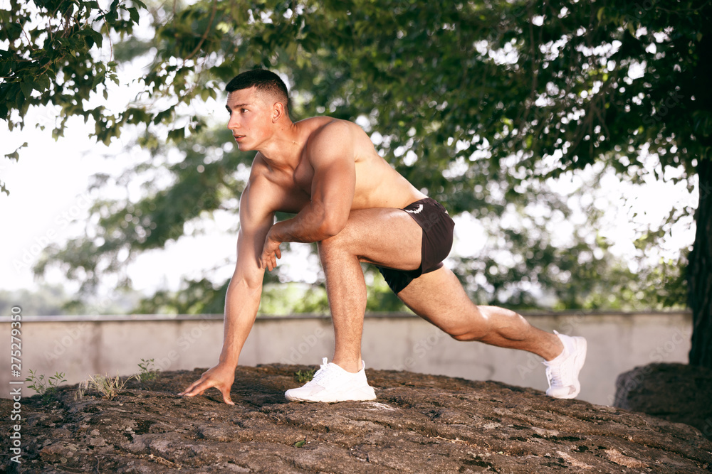 A muscular male athlete doing workout at the park. Gymnastics, training, fitness workout flexibility. Summer city in sunny day on background field. Active and healthy lifestyle, youth, bodybuilding. A muscular male athlete doing workout at the park. Gymnastics, training, fitness workout flexibility. Summer city in sunny day on background field. Active and healthy lifestyle, youth, bodybuilding.