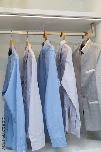 Wardrobe with stylish bag and clothes indoors. Clothes hanging on rail in white wardrobe