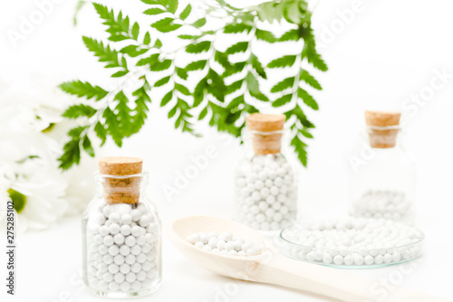 selective focus of pills in glass bottles with wooden corks near green leaves on white