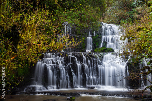 Purakaunui falls waterfall located in a serene forest. The Purakaunui Falls are a cascading three-tiered waterfall on the Purakaunui River, in The Catlins region of the South Island, New Zealand.