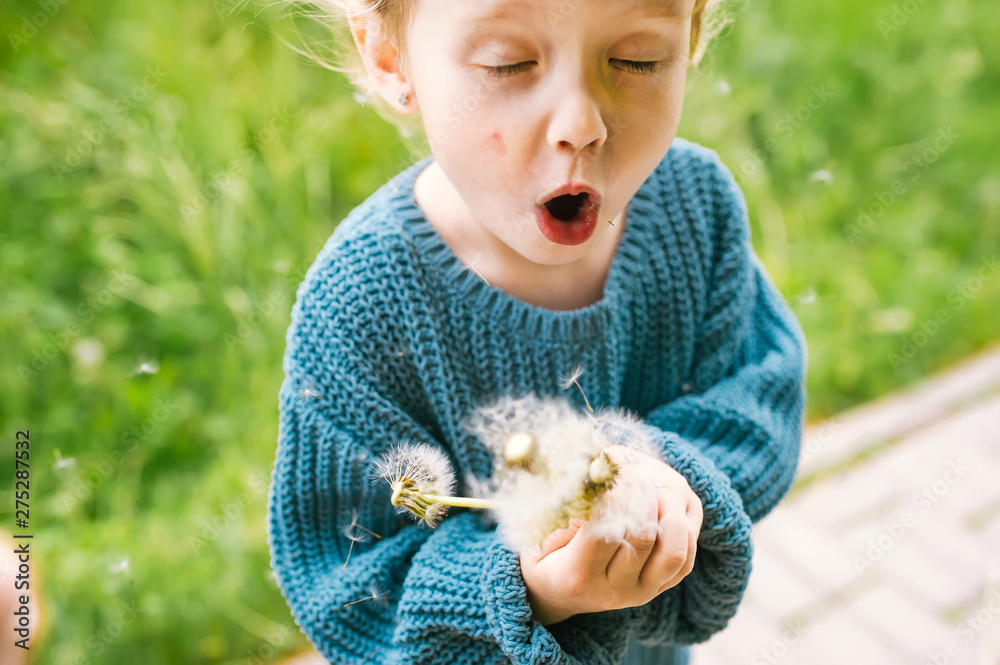 Φωτογραφία Caucasian baby girl blows on a dandelion flower in a park.