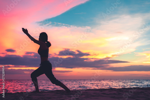 Sport Young woman silhouette practicing yoga on the sea beach at sunset