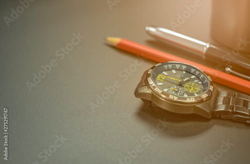 Close up shot of Black stainless steel watch with pen and red pencil On black metal surface background.