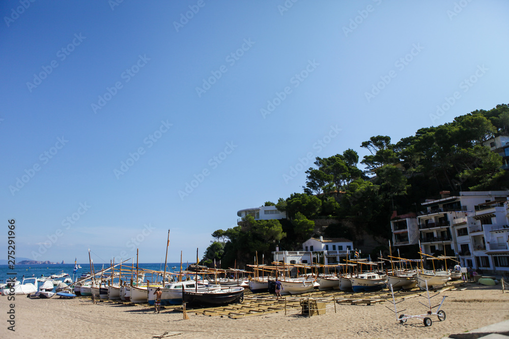 Traditional fishing boats standing in the shore. Small fisherman's village in Catalonia, Spain. Wooden boats on the bay, Mediterranean sea. White buildings are on the background. Summer vacations