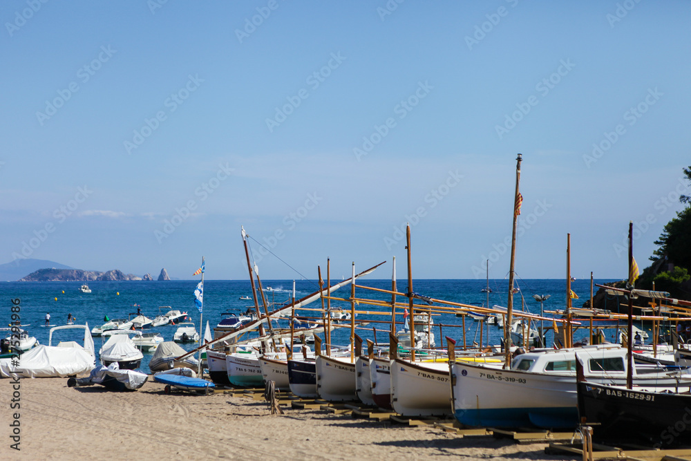 Traditional fishing boats standing in the shore. Small fisherman's village in Catalonia, Spain. Wooden boats on the bay, Mediterranean sea. White buildings are on the background. Summer vacations