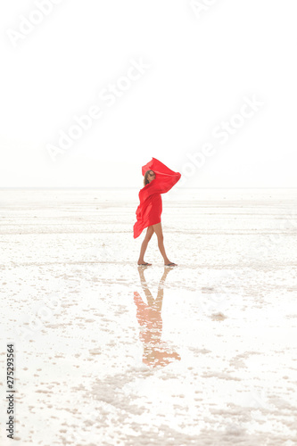 A girl in a coral swimsuit on the background of the salty sea of the lake. A girl with a floating cloth and a reflection in the water. Woman alone with nature in a swimsuit
