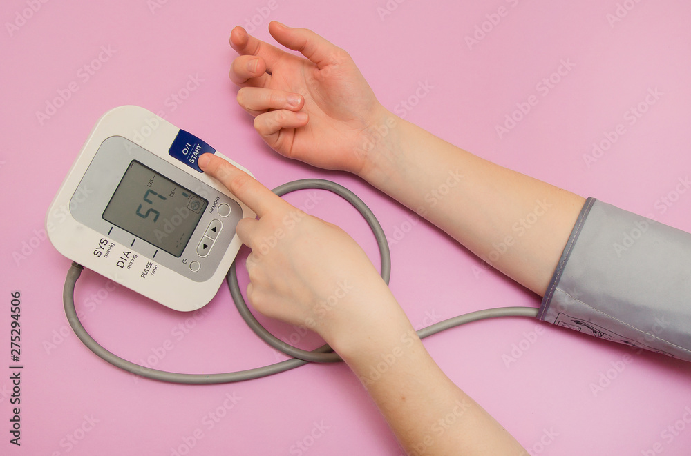 Measurement of pressure. The woman takes care of her health by checking her blood pressure and pulse on her arm. lilac background Measurement of pressure. The woman takes care of her health by checking her blood pressure and pulse on her arm. lilac background