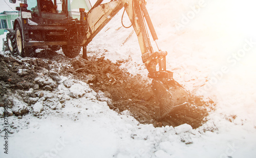 digging the earth in winter. Tractor works on the construction site in the cold winter Construction and snow removal equipment at the plant - loader with snow unloading during roadworks