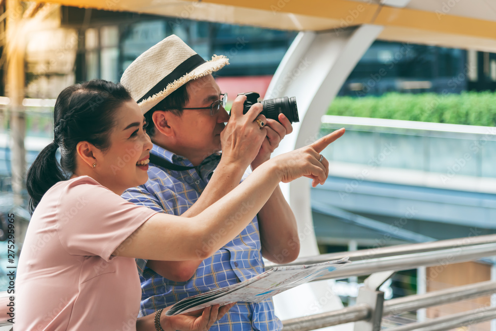 Asian couple retirement age,  tourists are happy With photography Various tourist attractions By looking at the map That the wife holds in her hand, to travel and elderly concept.